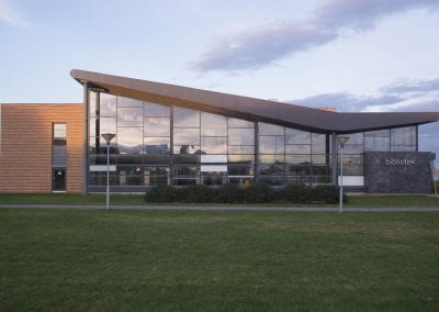 Foto av Vadsø bibliotekbygg, med moderne arkitektur og en fasade av glass, stein og tre.